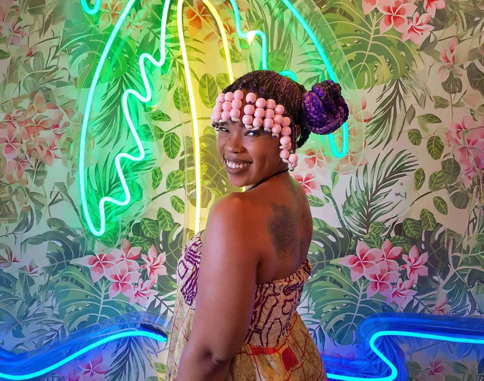 Bonolo smiling over her shoulder in front of a neon palm tree and a tropical wallpaper